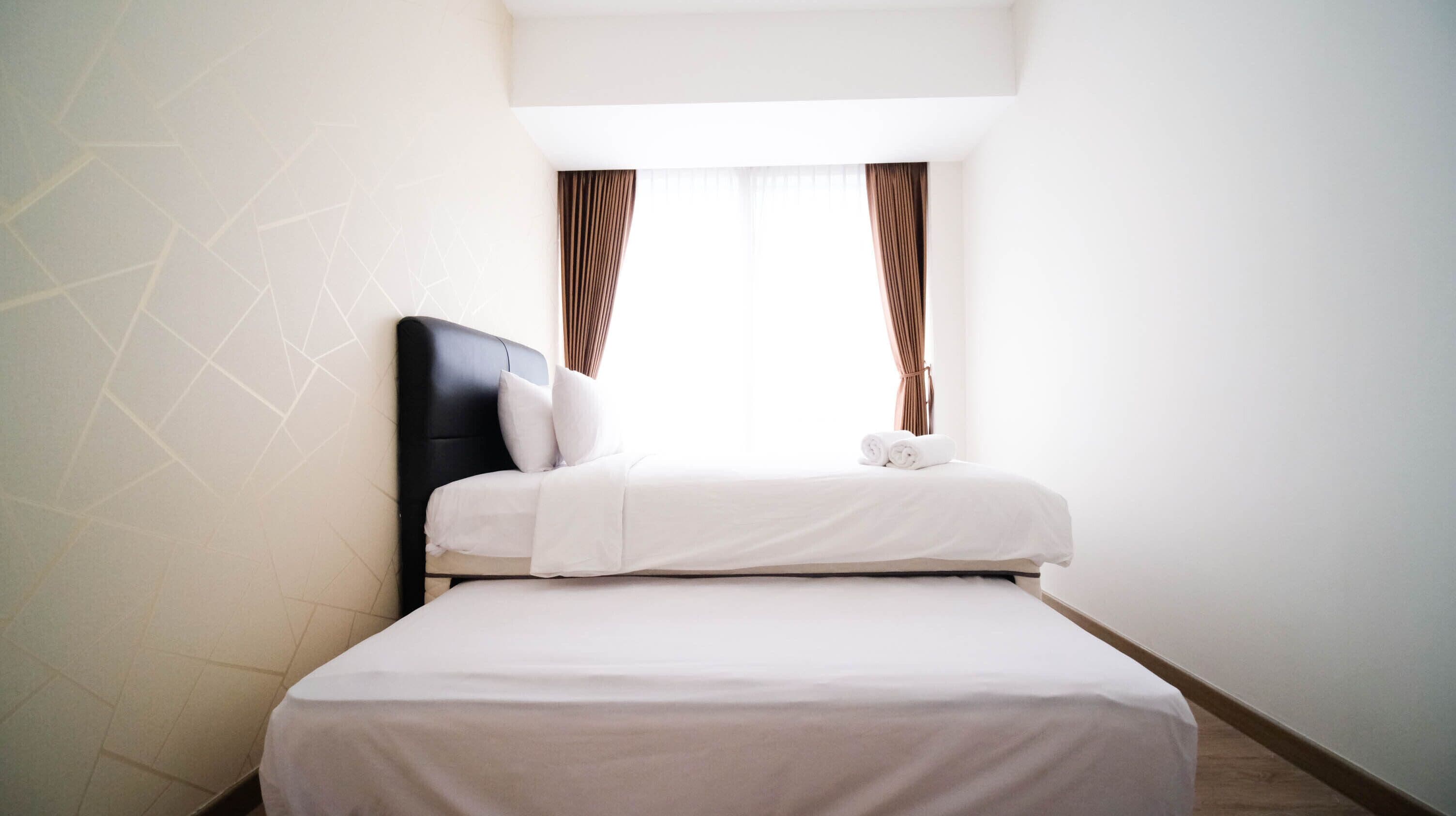A neatly made bed with white linens, a black headboard, and two brown curtains.