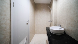 A modern bathroom with a white door, a black countertop, a white sink, and a shower with a handheld showerhead. - Nice 3Br Connected To Mall At Grand Sungkono Lagoon Apartment (Surabaya)