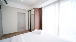 A hotel room with a bed, a door, a mirror, and a window with curtains. - Nice 3Br Connected To Mall At Grand Sungkono Lagoon Apartment (Surabaya)