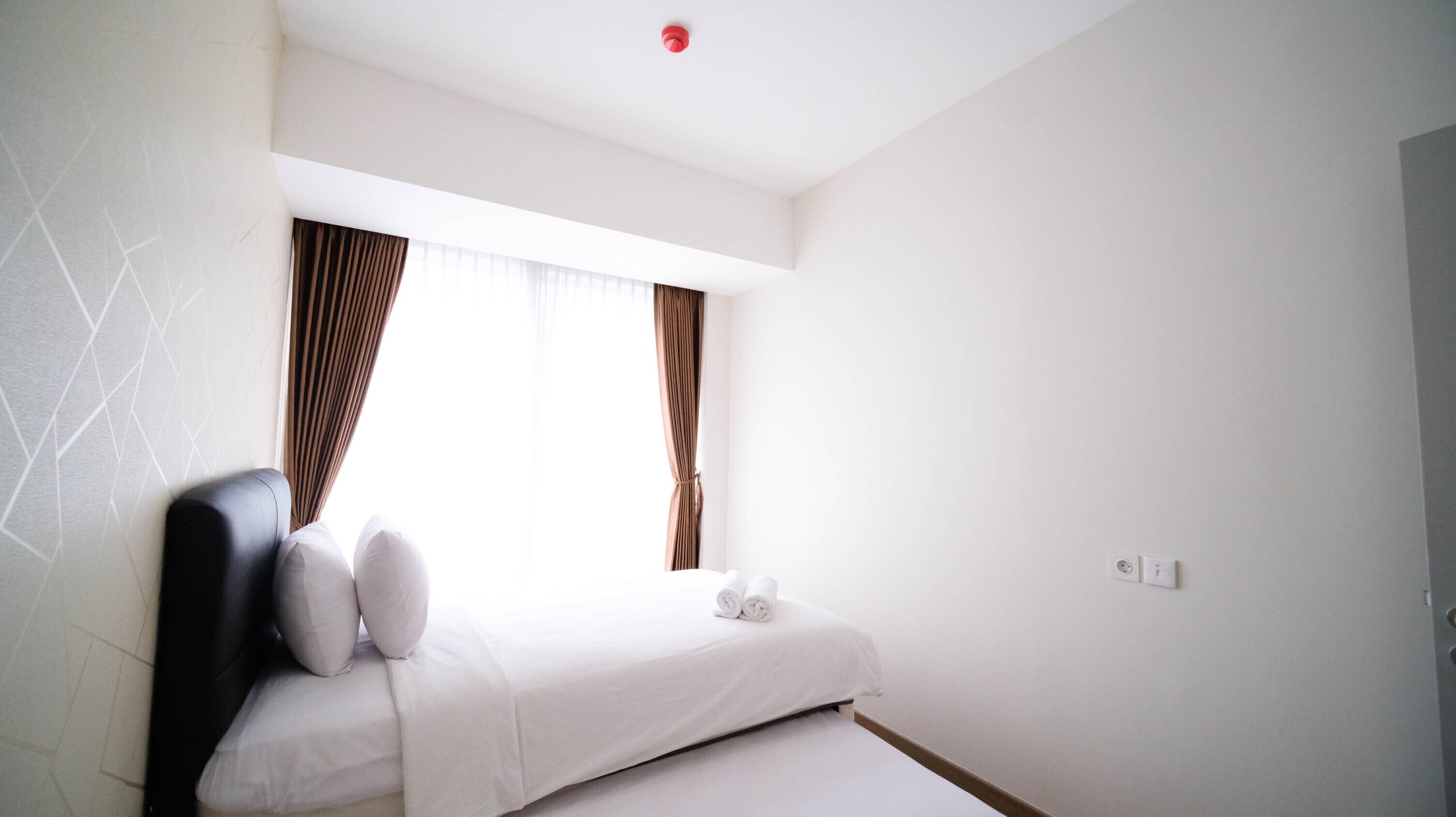 A minimalist hotel room with a bed, curtains, and a ceiling light.