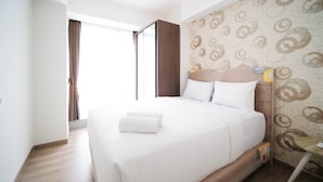 A neatly made bed with white linens and a folded towel, a wooden headboard, and a patterned wall. - Nice 3Br Connected To Mall At Grand Sungkono Lagoon Apartment (Surabaya)