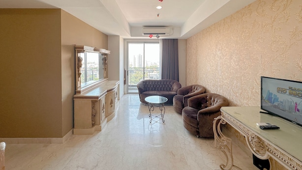 A spacious living room with a large window, a sofa, a TV, and a marble floor. - Nice 3Br Connected To Mall At Grand Sungkono Lagoon Apartment (Surabaya)