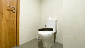 A small, clean bathroom with a toilet, a wooden door, and a white tiled wall. - Simply Studio Room LRT City Jatibening Apartment (Bekasi)