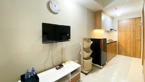 A modern kitchen with a flat-screen TV mounted on the wall, a built-in oven, and a wooden cabinet. - Simply Studio Room LRT City Jatibening Apartment (Bekasi)