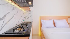 A modern hotel room with a marble wall, a black countertop with a stove, and a bed with white bedding.