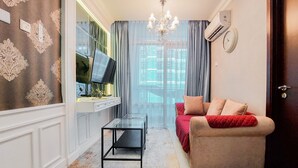 A living room with a sofa, a glass coffee table, a TV, and a chandelier. - Comfort Designed 1Br At Brooklyn Alam Sutera Apartment (South Tangerang)