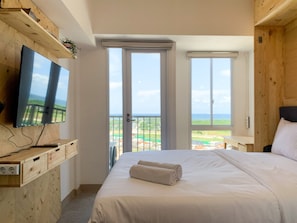 Quarto com cama, televisão fixada numa parede de madeira e varanda com vista.
