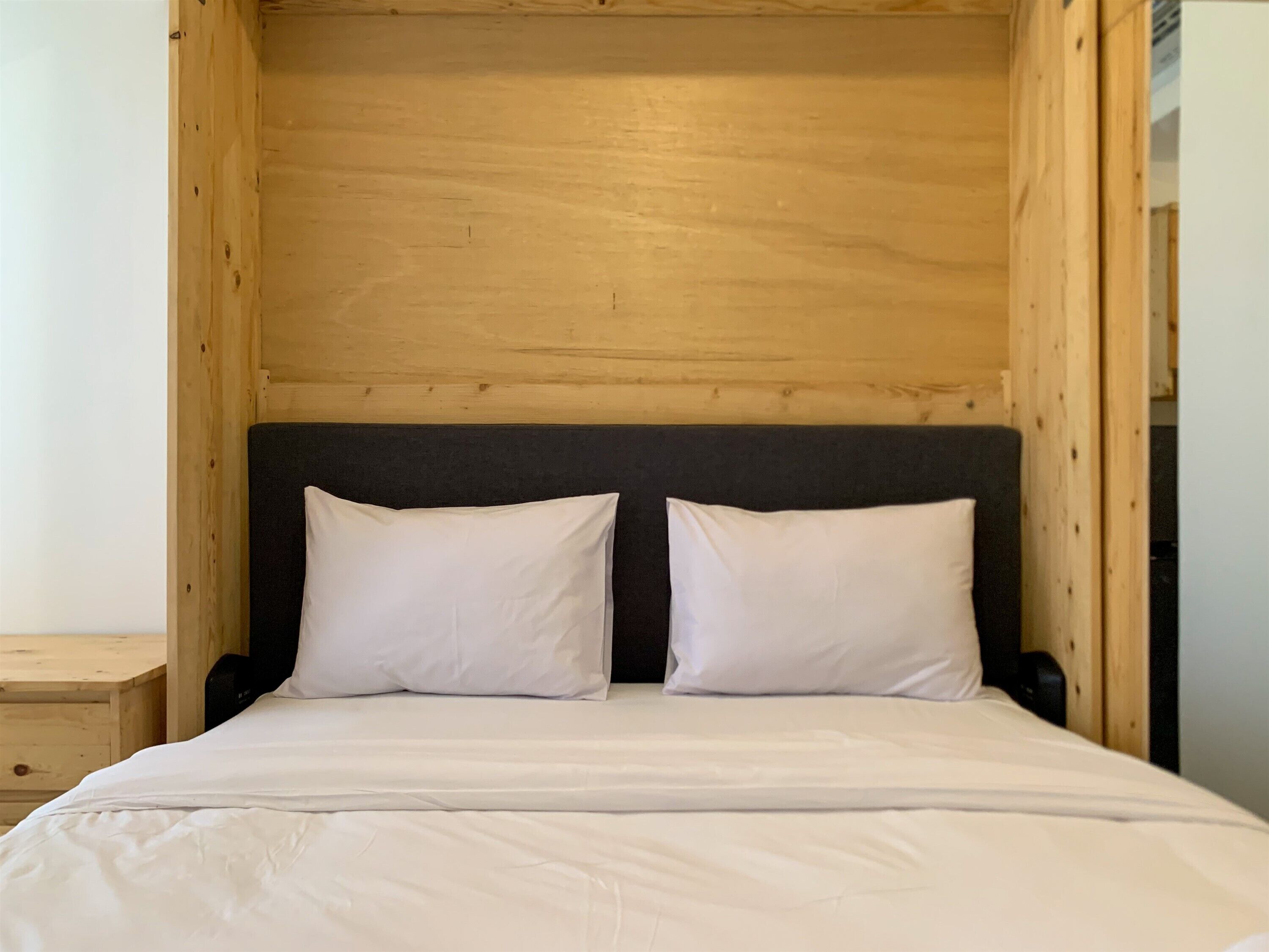 Un lit avec une literie blanche, dans une pièce aux murs en bois et dotée d’une tête de lit sombre.