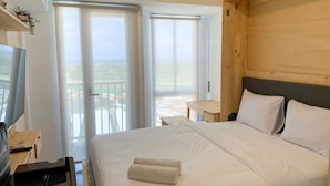 Ein Schlafzimmer mit einem großen Bett, einem Holzkopfende, einem Fernseher und einem Balkon mit Blick.