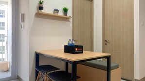 A small room with a wooden table, two black chairs, a shelf with plants, and a travel kit on the table. - Relaxing 2Br At 35Th Floor Tokyo Riverside Pik 2 Apartment (Teluknaga)