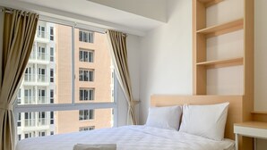 A hotel room with a bed, a nightstand, and a view of a building through the window. - Relaxing 2Br At 35Th Floor Tokyo Riverside Pik 2 Apartment (Teluknaga)