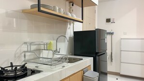 A modern kitchen with white tiles, a stainless steel sink, a black refrigerator, and a dish rack. - Relaxing 2Br At 35Th Floor Tokyo Riverside Pik 2 Apartment (Teluknaga)