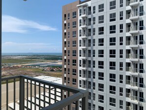 A high-rise residential building with multiple balconies, a clear view of the surrounding landscape, and a distant body of water.