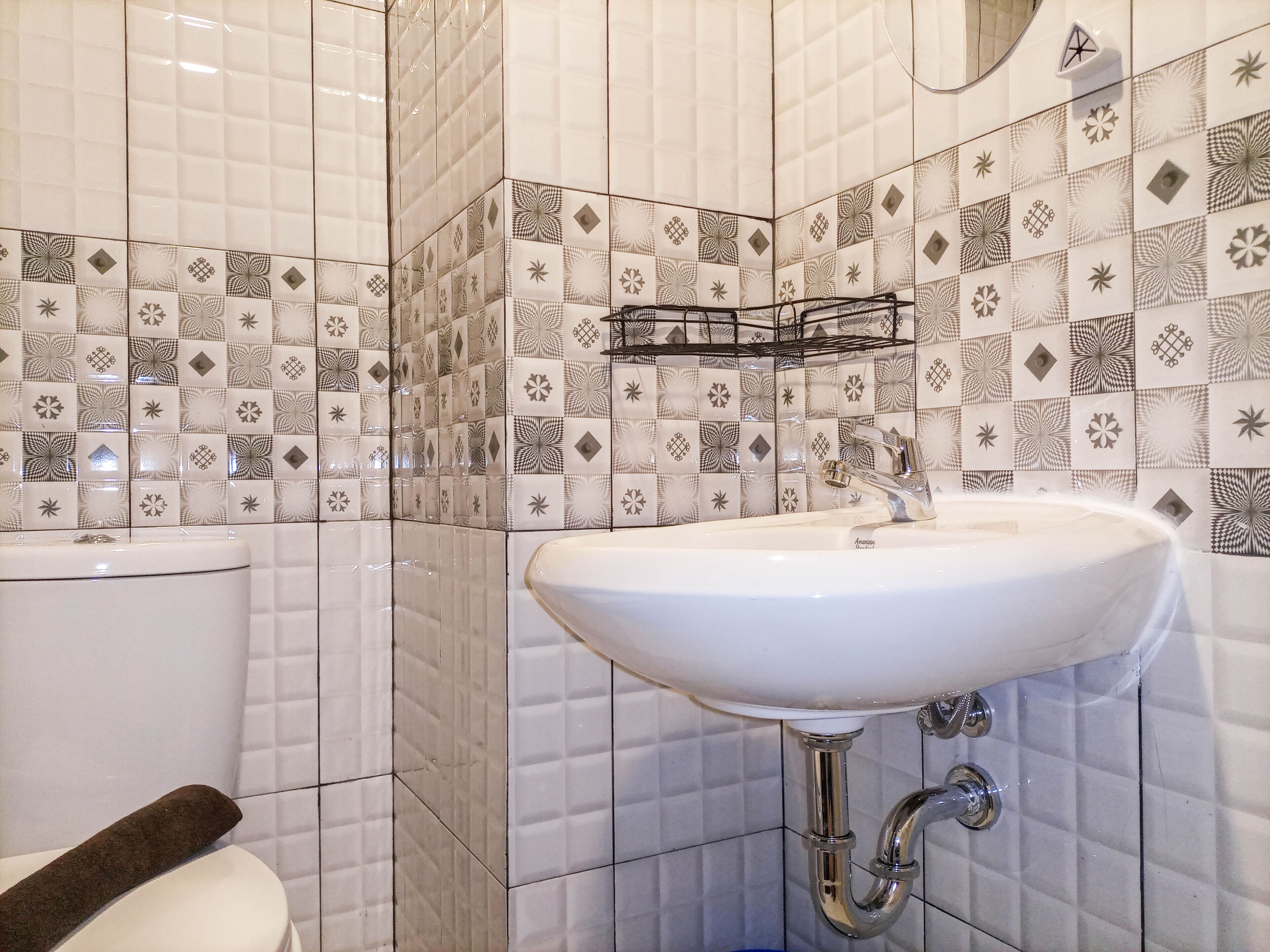 A bathroom with a white sink, a toilet, and a tiled wall with geometric patterns.