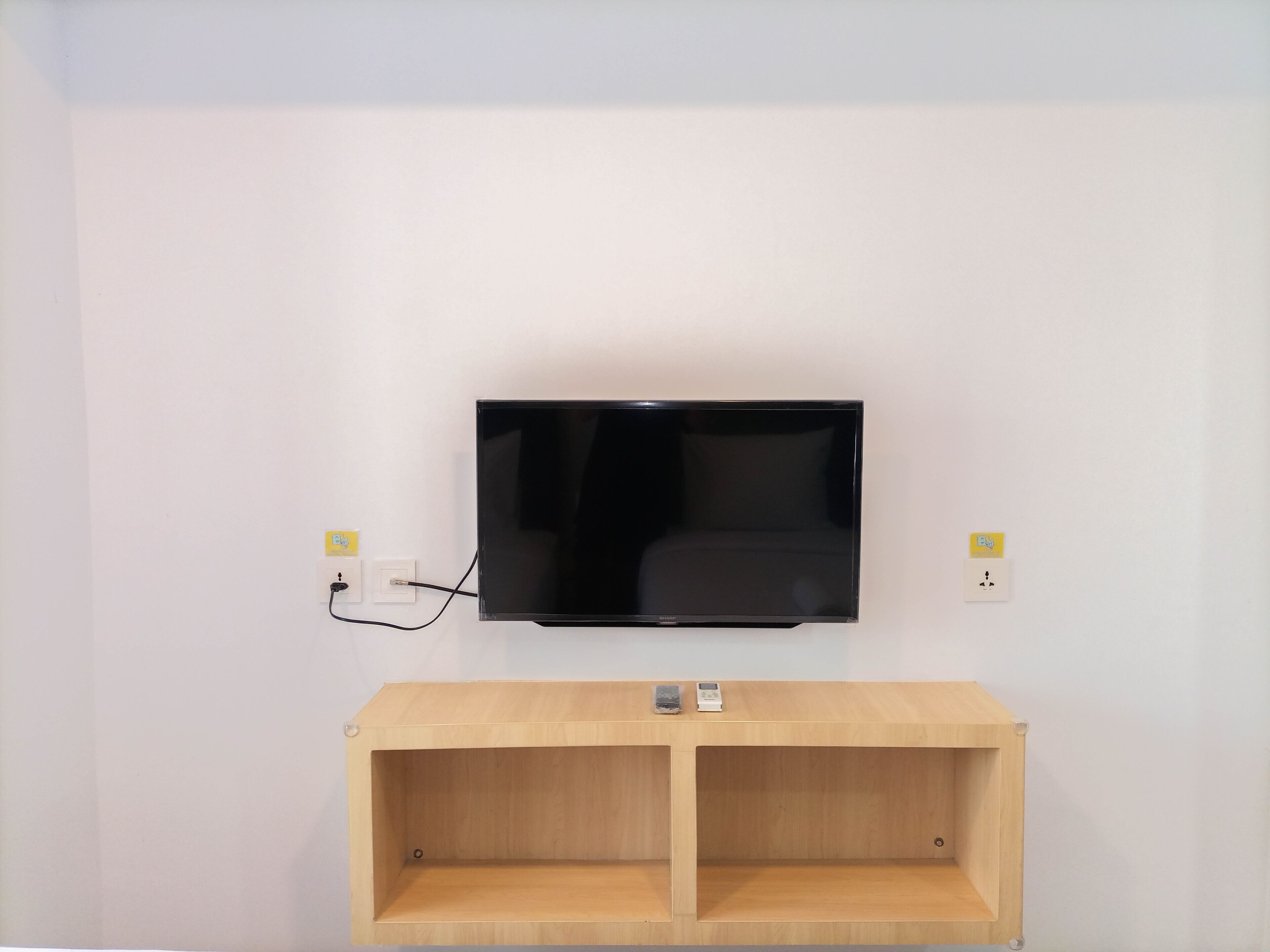 A flat-screen TV mounted on a white wall with a wooden console below.