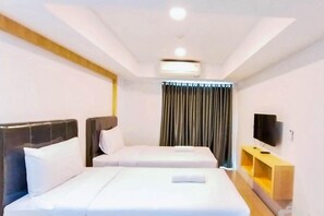 A hotel room with two beds, a flat-screen TV, a wooden nightstand, and a window with curtains. - Cozy Stay Studio At De Prima Apartment (Medan)