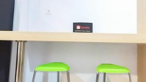 A traveler's desk area with a sign for 'Travelio' and two green chairs. - Comfort Studio At De Prima Apartment (Medan)