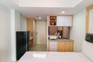 Una habitación de hotel compacta con una cama, una kitchenette pequeña, un refrigerador y un armario de madera.