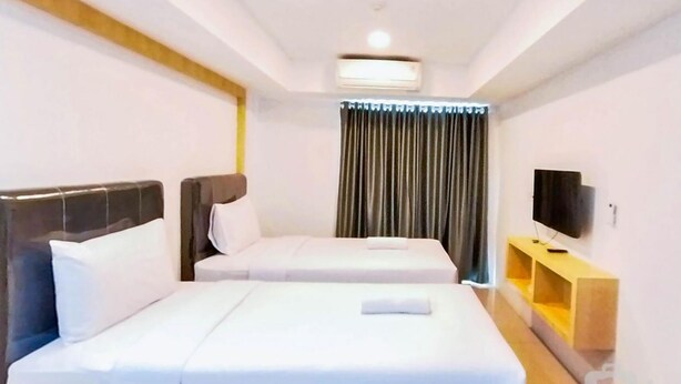 A hotel room with two beds, a flat-screen TV, a wooden nightstand, and a window with curtains. - Comfort Studio At De Prima Apartment (Medan)