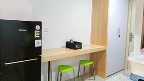 A compact kitchenette with a black refrigerator, a wooden countertop, two green stools, and a white wardrobe. - Comfort Studio At De Prima Apartment (Medan)