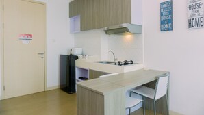 A compact kitchen with a built-in stove, a sink, and a small dining area with a chair. - Cozy Living Studio Apartment Tree Park City Bsd (South Tangerang)