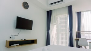 Ein Hotelzimmer mit einem Bett, einem an der Wand montierten Fernseher, einem Nachttisch mit Telefon und einem Fenster mit Vorhängen.