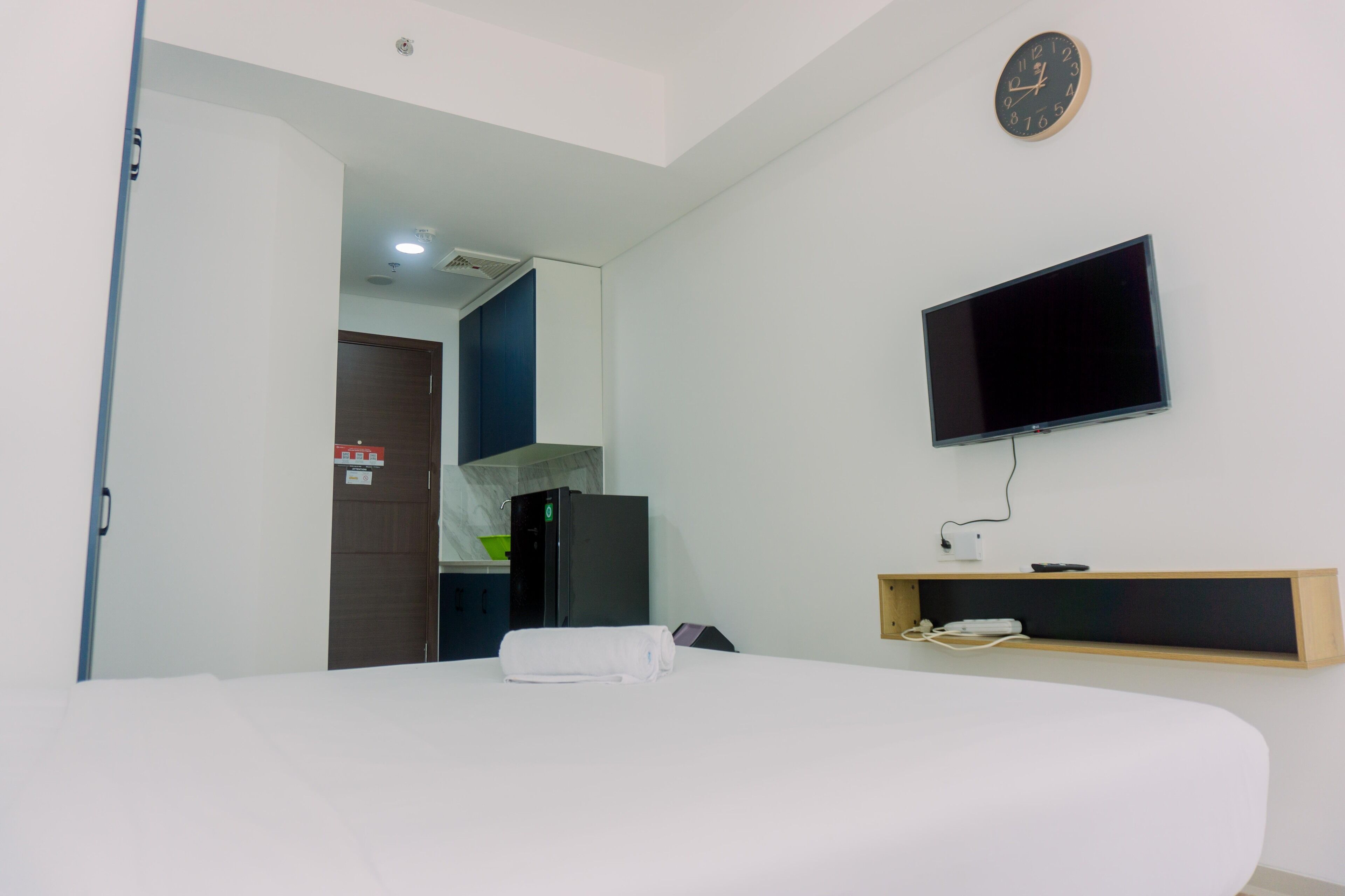 Une chambre d’hôtel avec un lit, un téléviseur fixé au mur, une petite étagère en bois et une porte donnant sur une salle de bain.