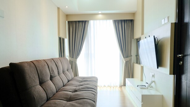A modern living room with a sofa, a flat-screen TV mounted on the wall, and a small table with a phone and charger.