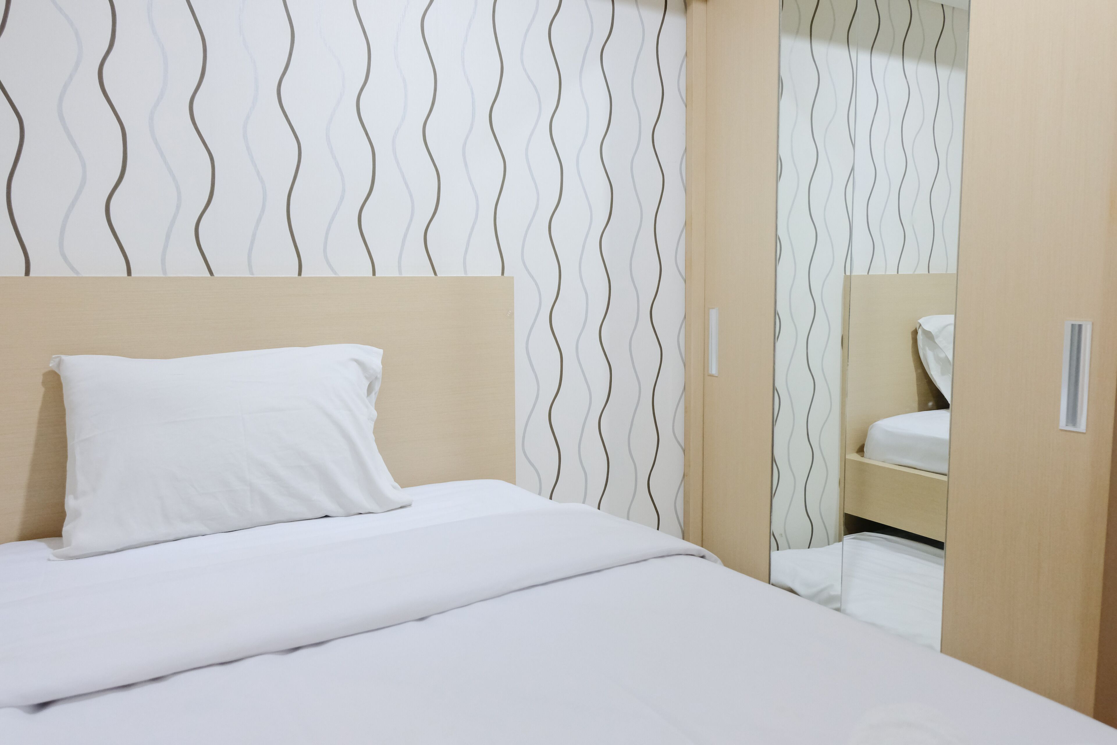Una cama bien tendida con sábanas blancas, cabecera de madera y pared con un estampado ondulado.