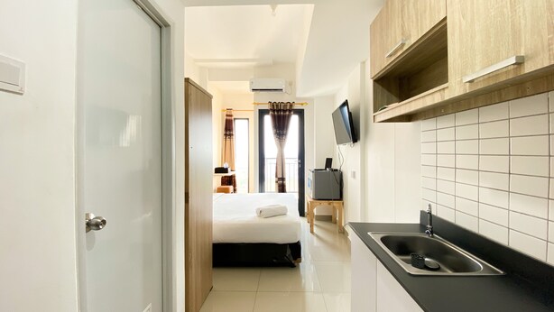 Una habitación de hotel compacta con kitchenette, cama, televisor y baño.