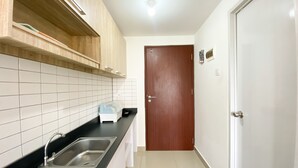 Una cocina con cubierta negra, pileta de acero inoxidable, armarios de madera y una puerta blanca.