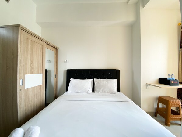 Une chambre d’hôtel avec un lit, une armoire, un petit tabouret et une étagère avec des bouteilles d’eau.