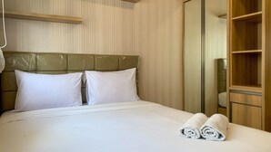 Ein ordentlich bezogenes Bett mit weißen Leinen und Kissen, ein Holz-Kopfteil und ein Holzschrank mit Spiegel.