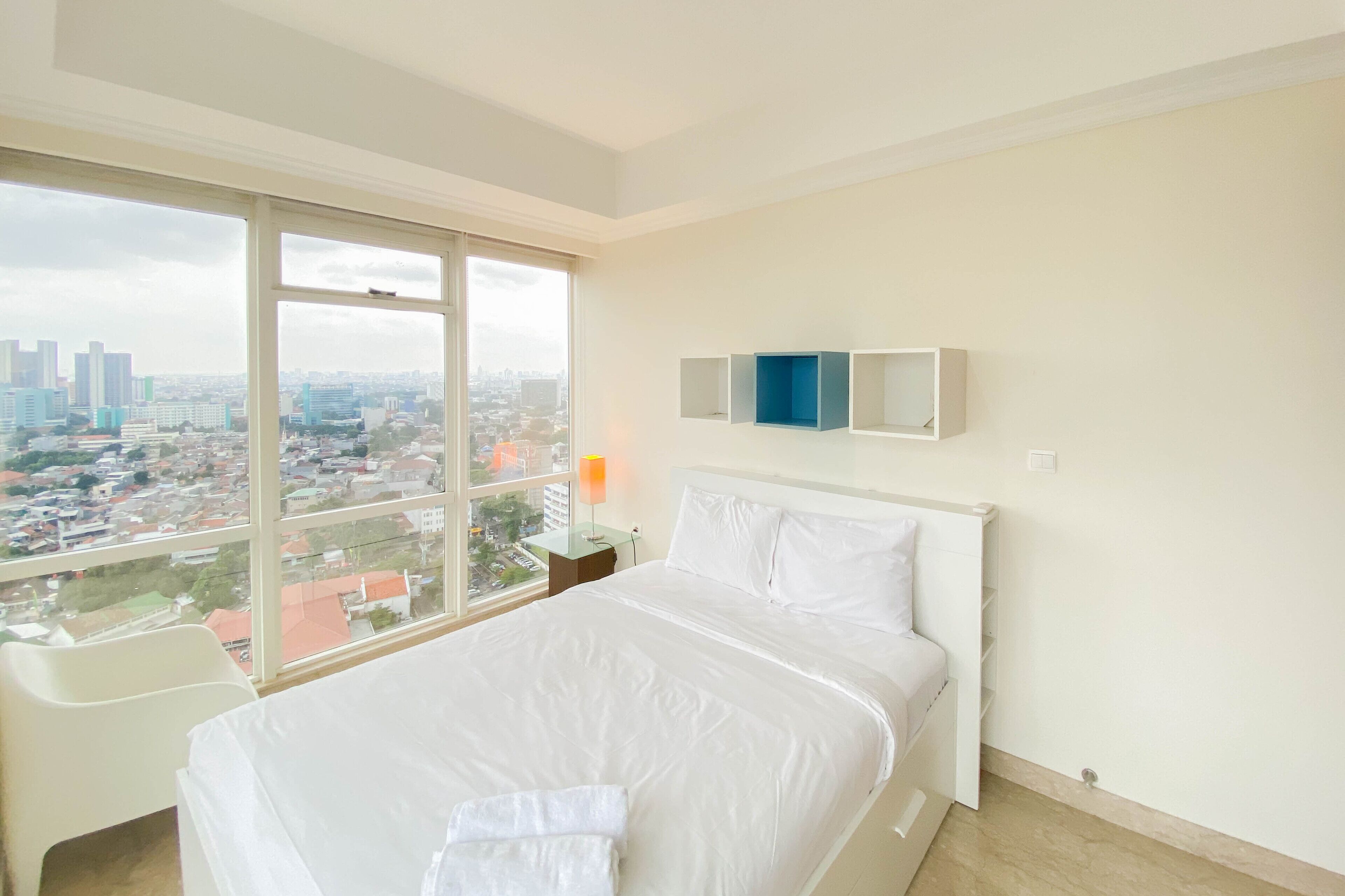 Habitación de hotel con una cama grande, un escritorio y vistas a un paisaje urbano a través de un ventanal amplio.