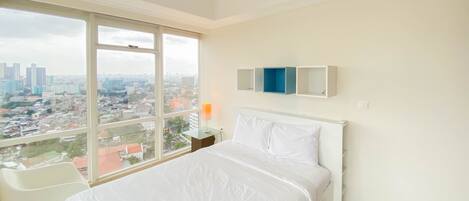 Habitación de hotel con una cama grande, un escritorio y vistas a un paisaje urbano a través de un ventanal amplio.