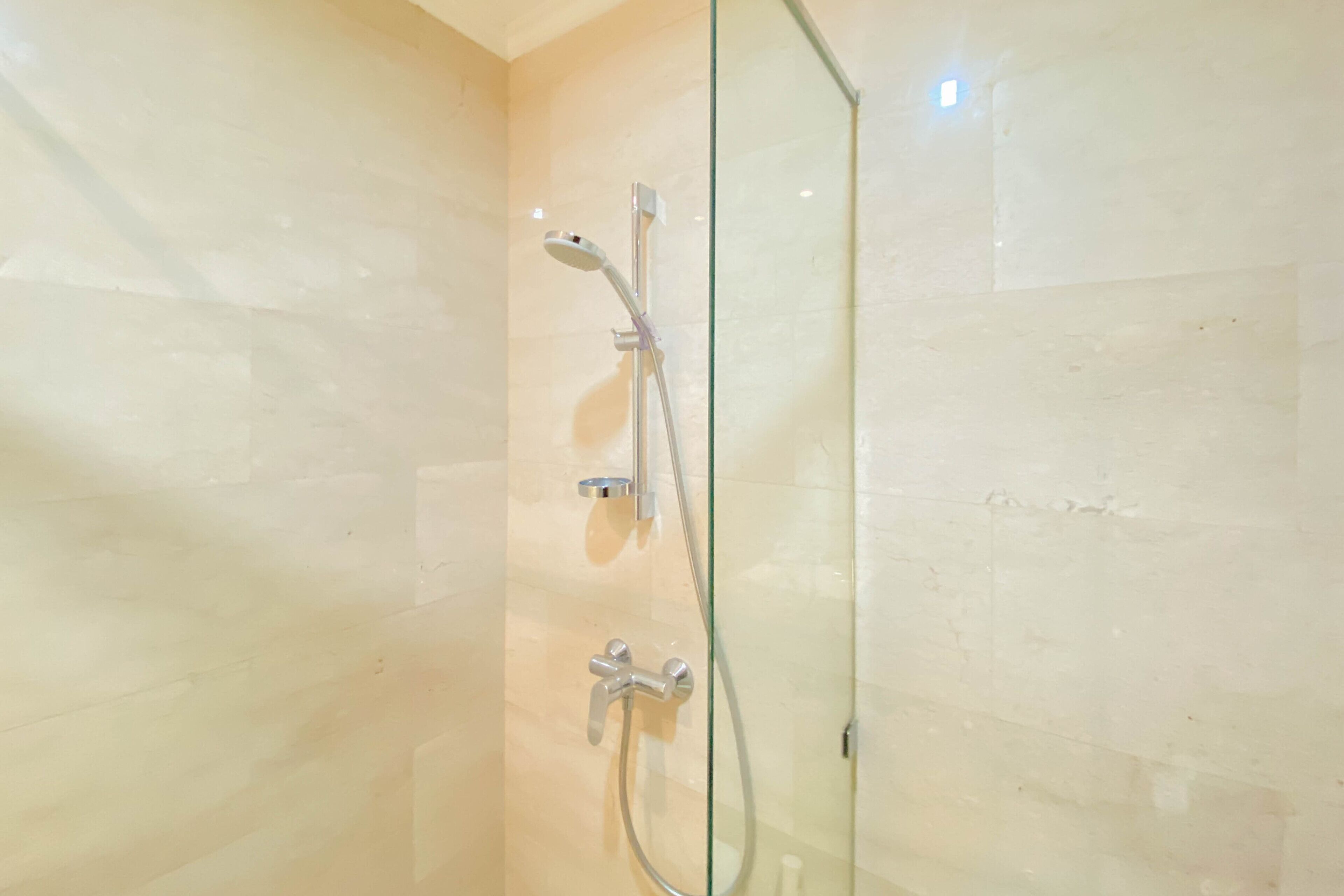 Eine begehbare Dusche mit Glaswand, einer Handbrause und einem am Wand montierten Wasserhahn.