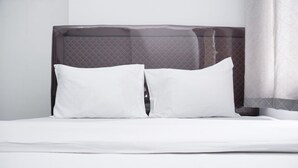 A neatly made bed with white linens and two pillows, a dark headboard, and sheer curtains.