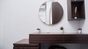 A modern vanity with a round mirror, a dark wooden dresser, and three potted plants.