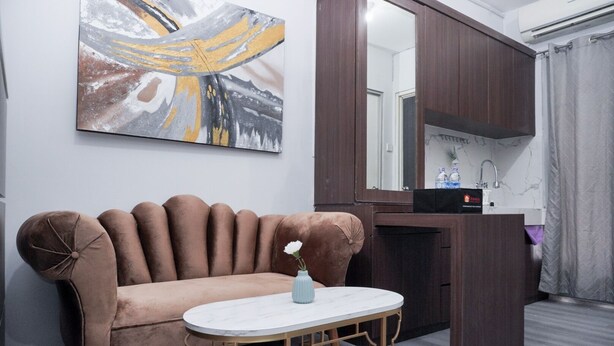 A modern living room with a brown sofa, a small round table with a vase, a large mirror, and a dark wooden cabinet.