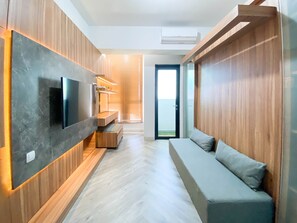 Ein modernes Wohnzimmer mit integriertem Fernseher, Holzvertäfelung, einem grauen Sofa und einer Glastür zum Balkon.