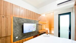 Habitación de hotel moderna con una cama grande, paneles de madera, un televisor de pantalla plana y un banco empotrado.