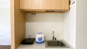 A compact kitchen with wooden cabinets, a built-in sink, a rice cooker, and a scale. - Comfy And Tidy Studio At Pollux Chadstone Apartment (Cikarang)