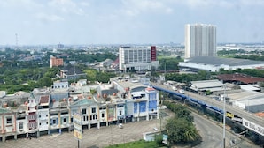 A cityscape with a mix of commercial and residential buildings, a prominent high-rise building, and a bridge. - Comfy And Tidy Studio At Pollux Chadstone Apartment (Cikarang)