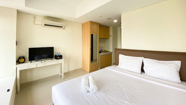 A hotel room with a bed, a desk with a television, and a kitchenette. - Comfy And Tidy Studio At Pollux Chadstone Apartment (Cikarang)
