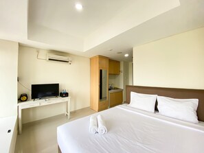 A hotel room with a bed, a desk with a television, and a kitchenette.