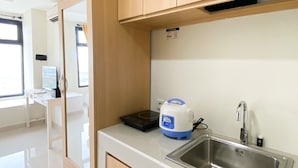 A modern kitchen with a stainless steel sink, a rice cooker, and a window with a view of buildings. - Comfy And Tidy Studio At Pollux Chadstone Apartment (Cikarang)