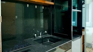 A modern kitchen with a black countertop, a built-in sink, and a wooden shelf above the sink. - Relaxing Studio At Vida View Makassar Apartment (Makassar)