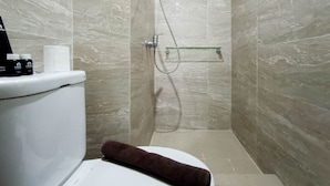A bathroom with a toilet, a glass shower enclosure, and a towel on the seat. - Relaxing Studio At Vida View Makassar Apartment (Makassar)