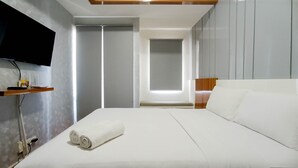 A modern hotel room with a large bed, a flat-screen TV mounted on the wall, and a wooden shelf with a remote control. - Relaxing Studio At Vida View Makassar Apartment (Makassar)