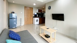 A modern living room with a sofa, a small wooden table, a washing machine, a refrigerator, and a kitchen in the background.